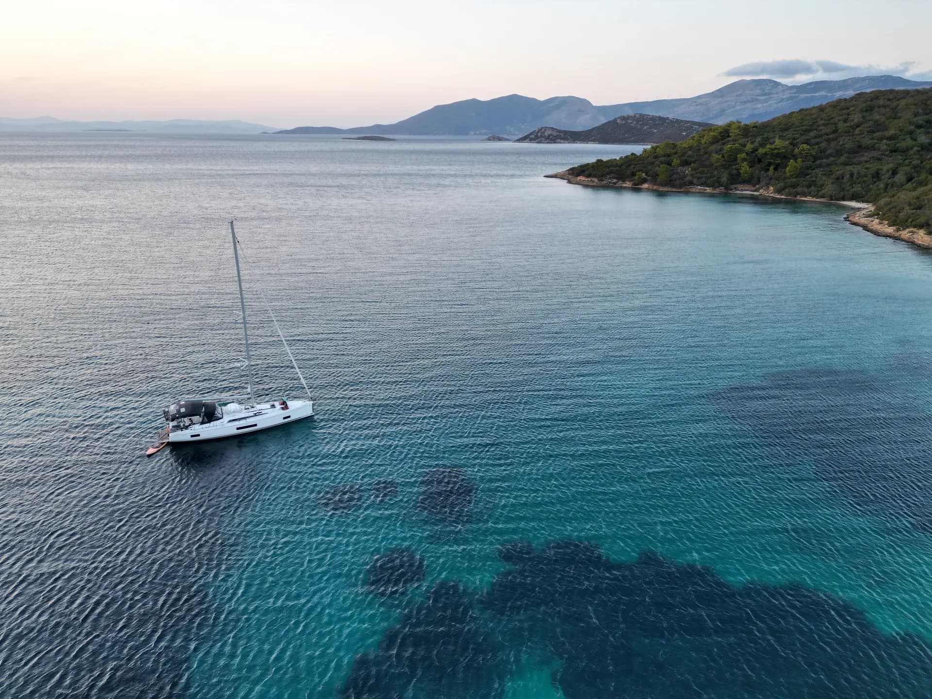 Drone shot of a lone Oceanis 46 anchored off the coast of a Cyclades island, late afternoon
